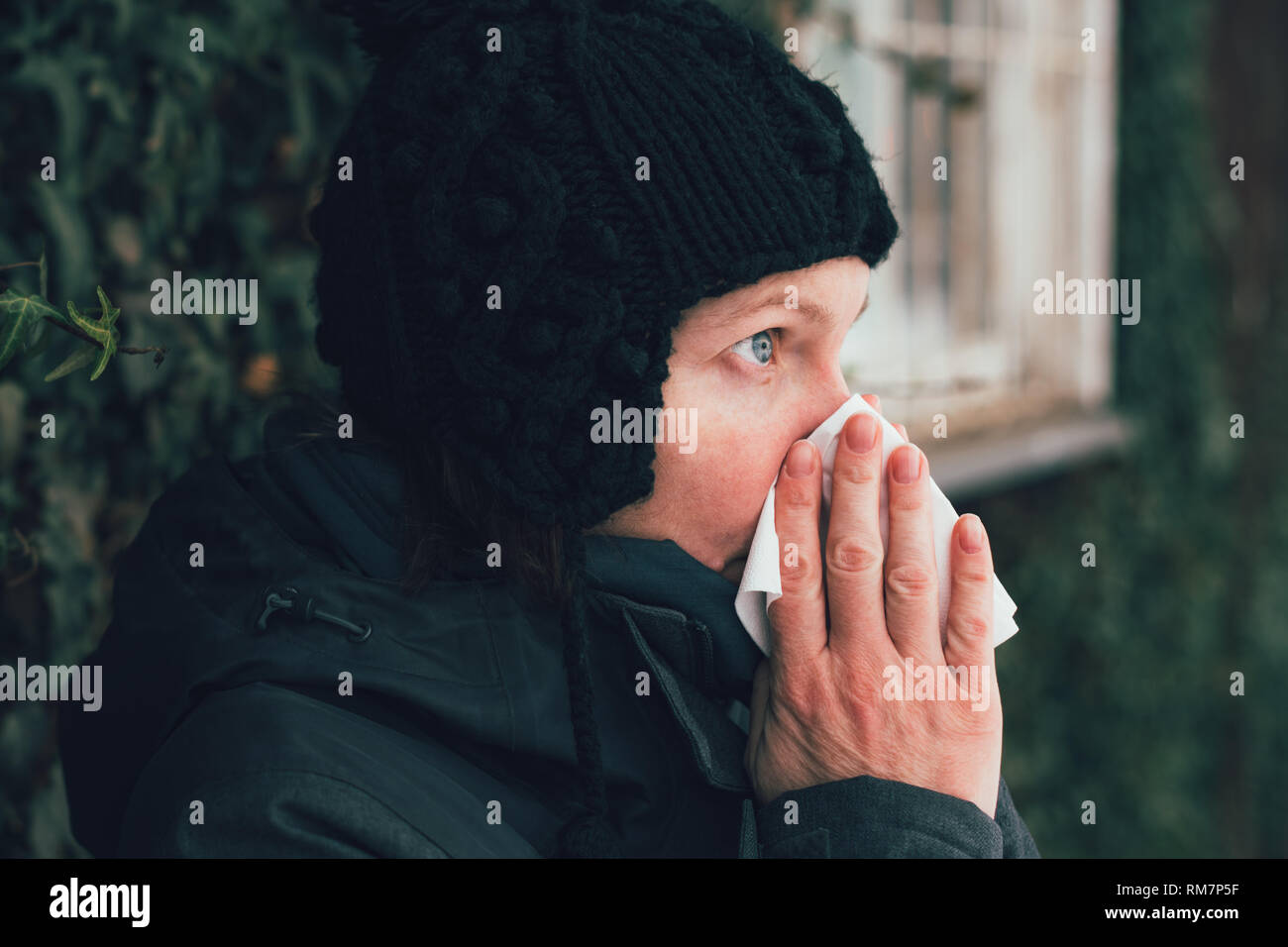 Donna soffia il naso in un fazzoletto di carta per strada in una fredda giornata invernale all'inizio della stagione influenzale Foto Stock