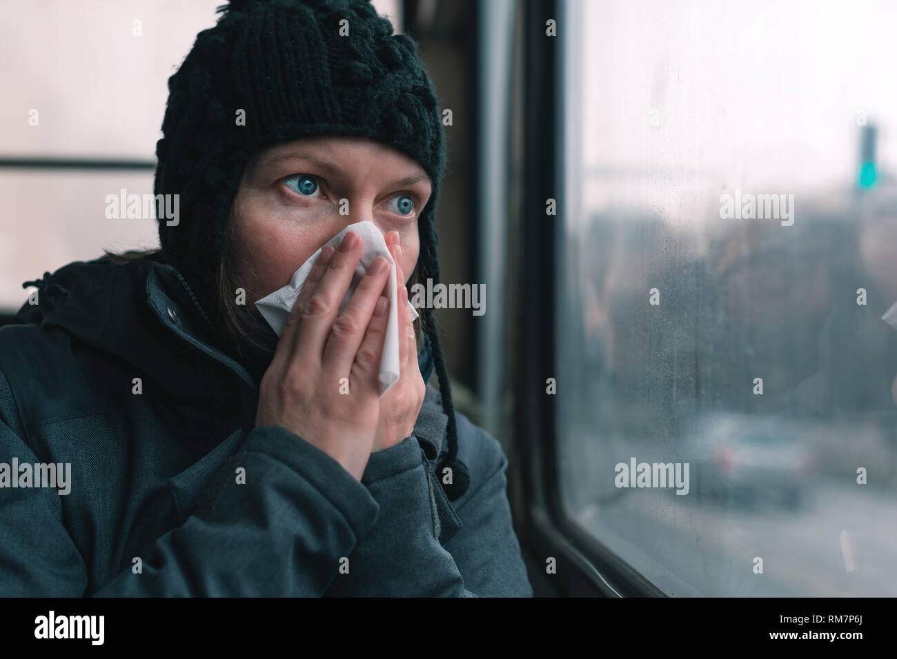 Donna soffia il naso in un fazzoletto di carta sul bus in una fredda giornata invernale all'inizio della stagione influenzale Foto Stock