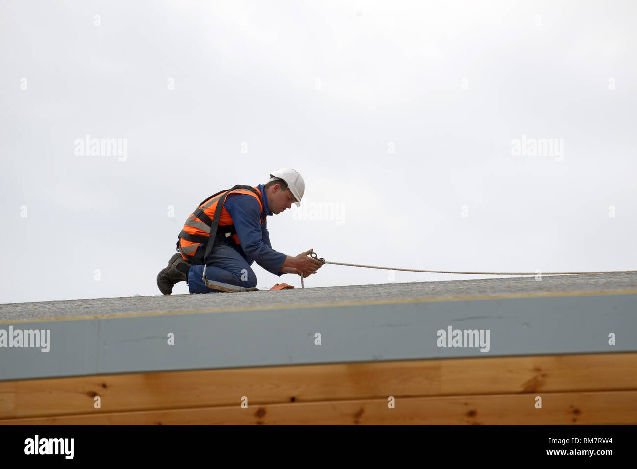 Un costruttore fissa linee di sicurezza per gli uomini circa a mettere il tetto su un grande edificio commerciale Foto Stock