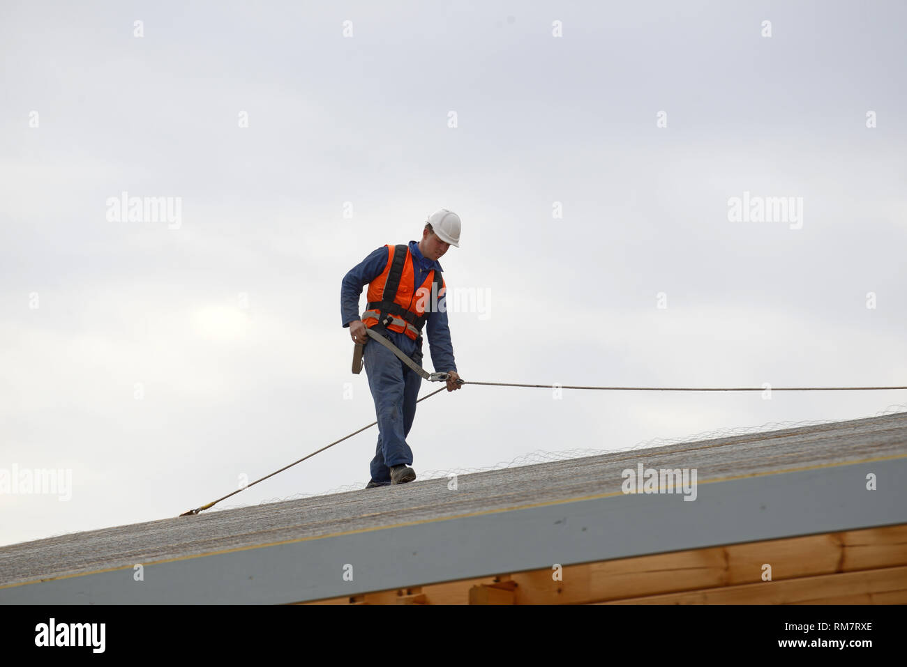 Un costruttore fissa linee di sicurezza per gli uomini circa a mettere il tetto su un grande edificio commerciale Foto Stock
