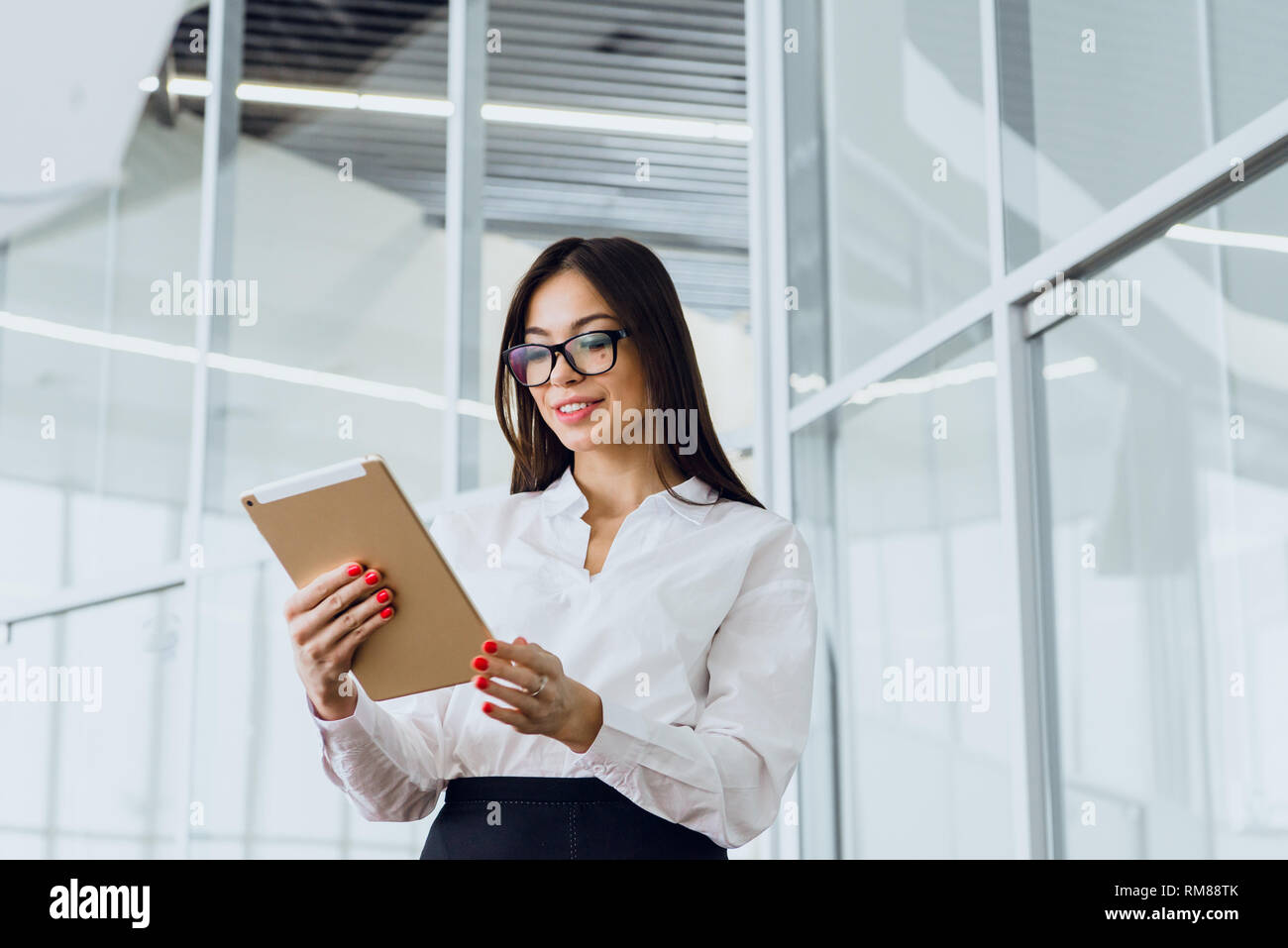 Giovane e bella donna d'affari guardando il suo tablet in un grande edificio aziendale Foto Stock