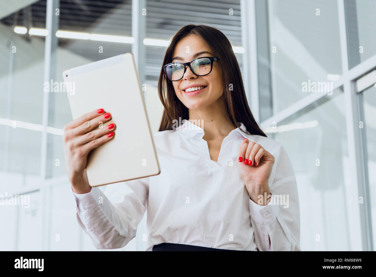 Attraente imprenditrice utilizzando una tavoletta digitale mentre in piedi in un grande edificio aziendale Foto Stock