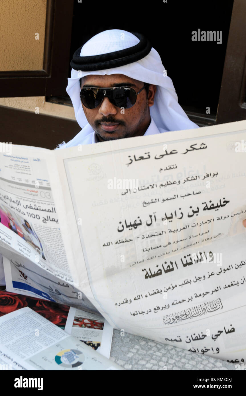 Un uomo Emirati in arabo tradizionale accappatoi e una carta bianca comune e nuova keffiyeh, rilassarsi leggendo il suo quotidiano in Dubai negli Emirati Arabi Uniti (EAU). Foto Stock