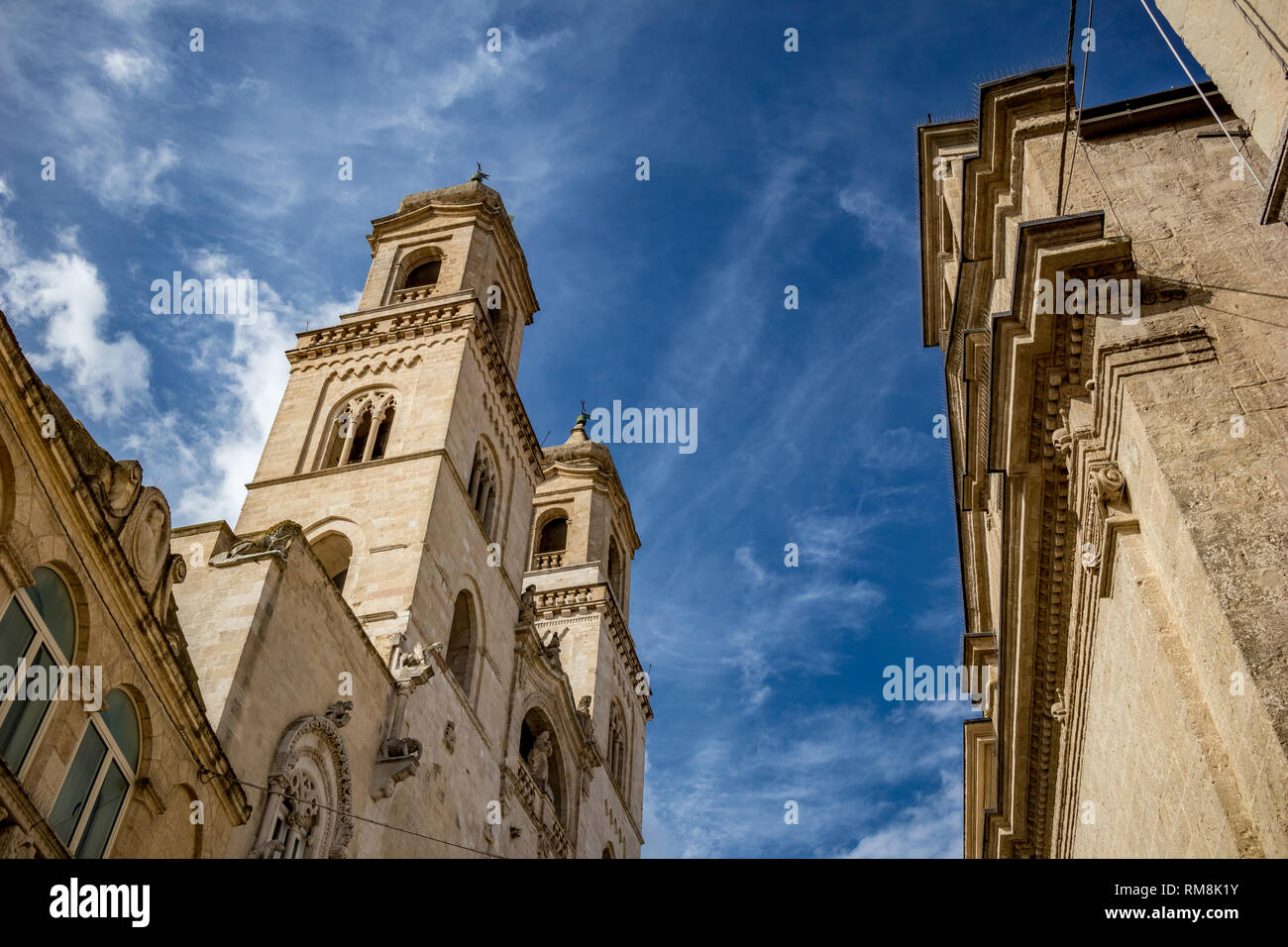 Strada laterale in vista della Cattedrale di Santa Maria Assunta e le sue facciate e le elevazioni nel paesaggio giornata estiva con cielo blu e puffy nuvole bianche. L'Italia, Regione Puglia, Altamura Foto Stock