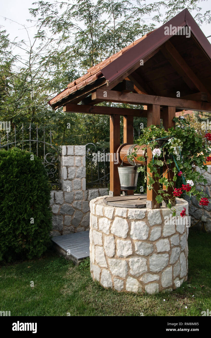 Il pozzo in pietra con un tetto di legno e un secchio di acqua nel  bellissimo giardino moderno Foto stock - Alamy