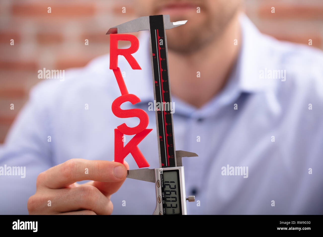 Mano umana di misurazione rischio rosso parola con elettronica digitale del calibro a corsoio Foto Stock