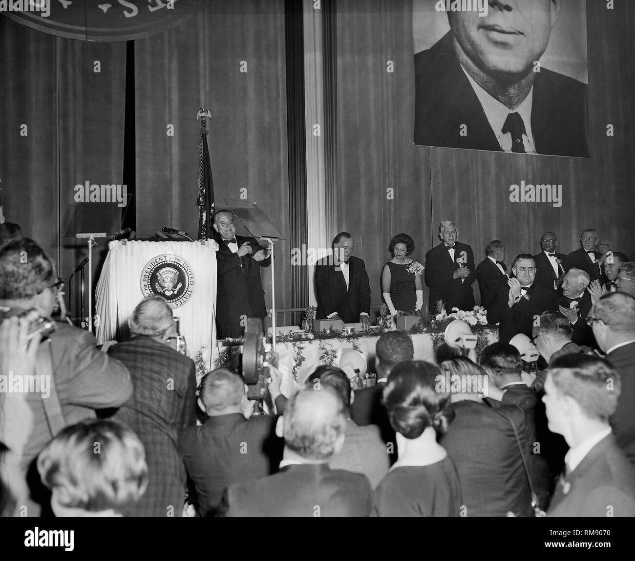 Il presidente Lyndon Johnson è applaudita dopo un discorso a Chicago sotto un grande ritratto di JFK, ca. 1964. Foto Stock