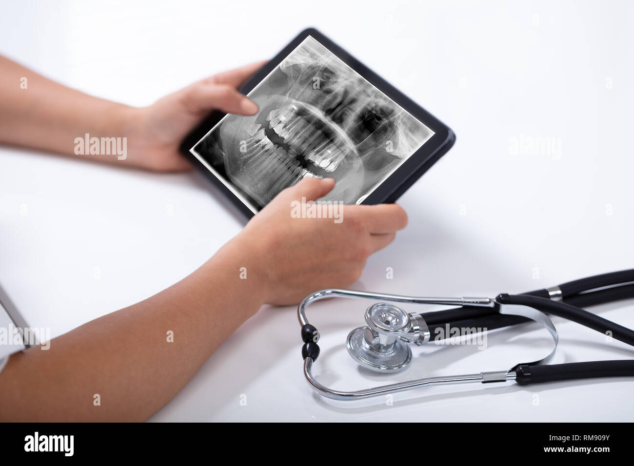 Close-up di medico tenendo tavoletta digitale con denti umani X-ray e uno stetoscopio su sfondo bianco Foto Stock