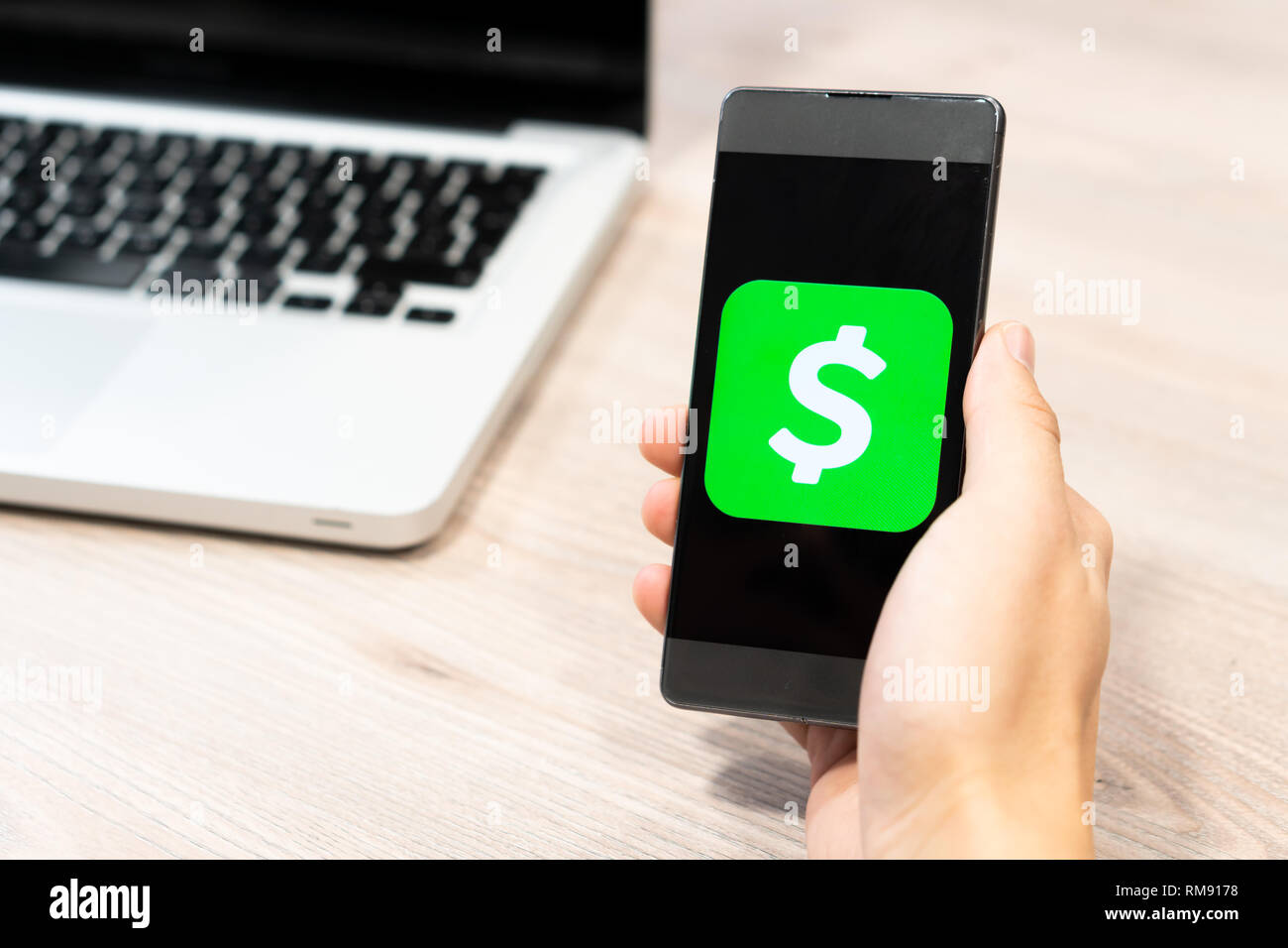 Cash logo App da Square inc visualizzate sullo smartphone detenute da mano umana accanto a computer laptop - Slovenia 13.02.2019 Foto Stock