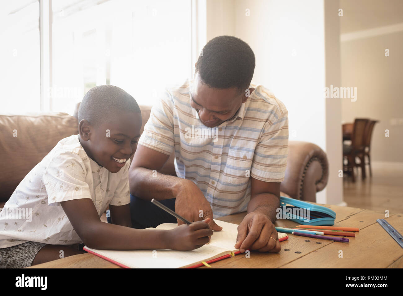 Vista frontale di African American padre aiutando il suo figlio con i compiti a tavola Foto Stock