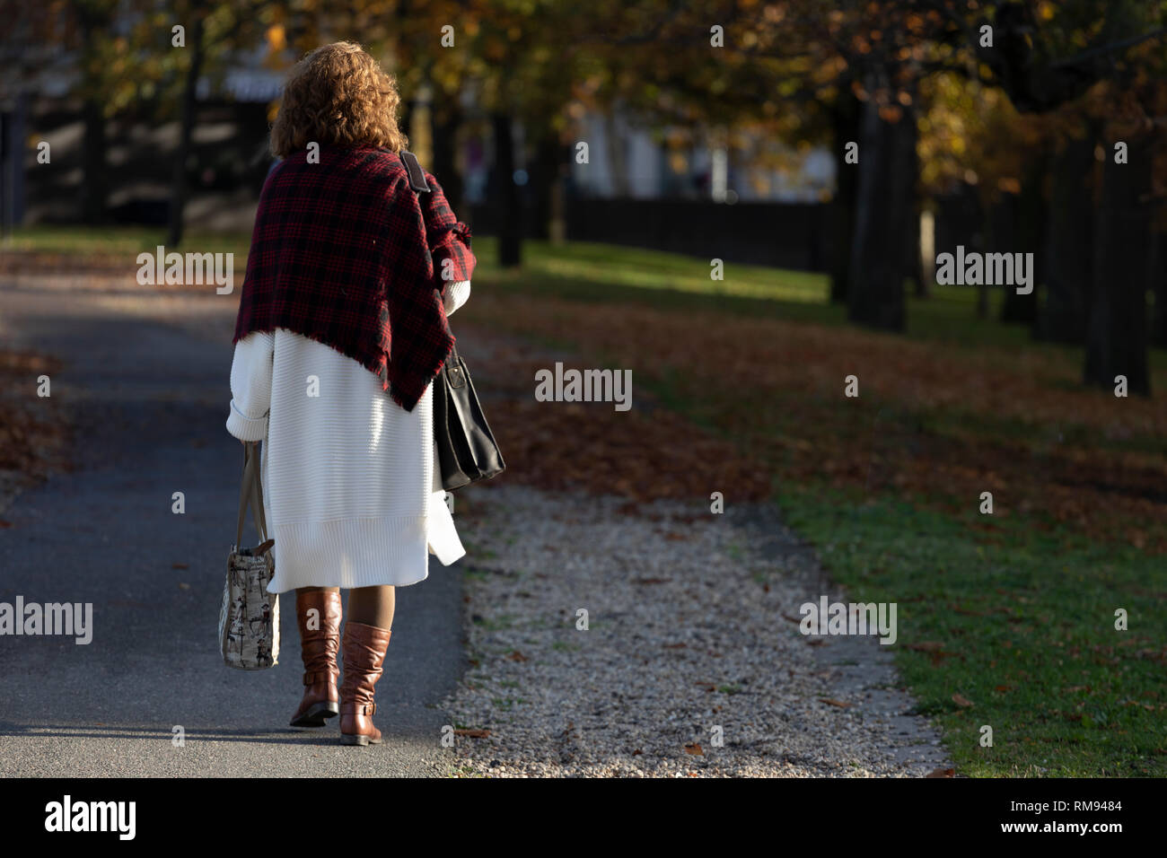 Elegante donna in autunno abbigliamento camminando giù per un sentiero in autunno con la luce solare bassa illuminare dal suo lato Foto Stock