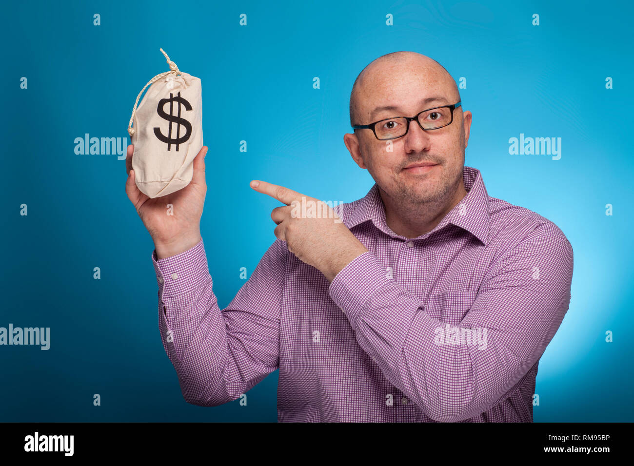 Un imprenditore in un spinaroli shirt puntando con il dito indice su un sacco di dollari, su sfondo blu. Foto Stock