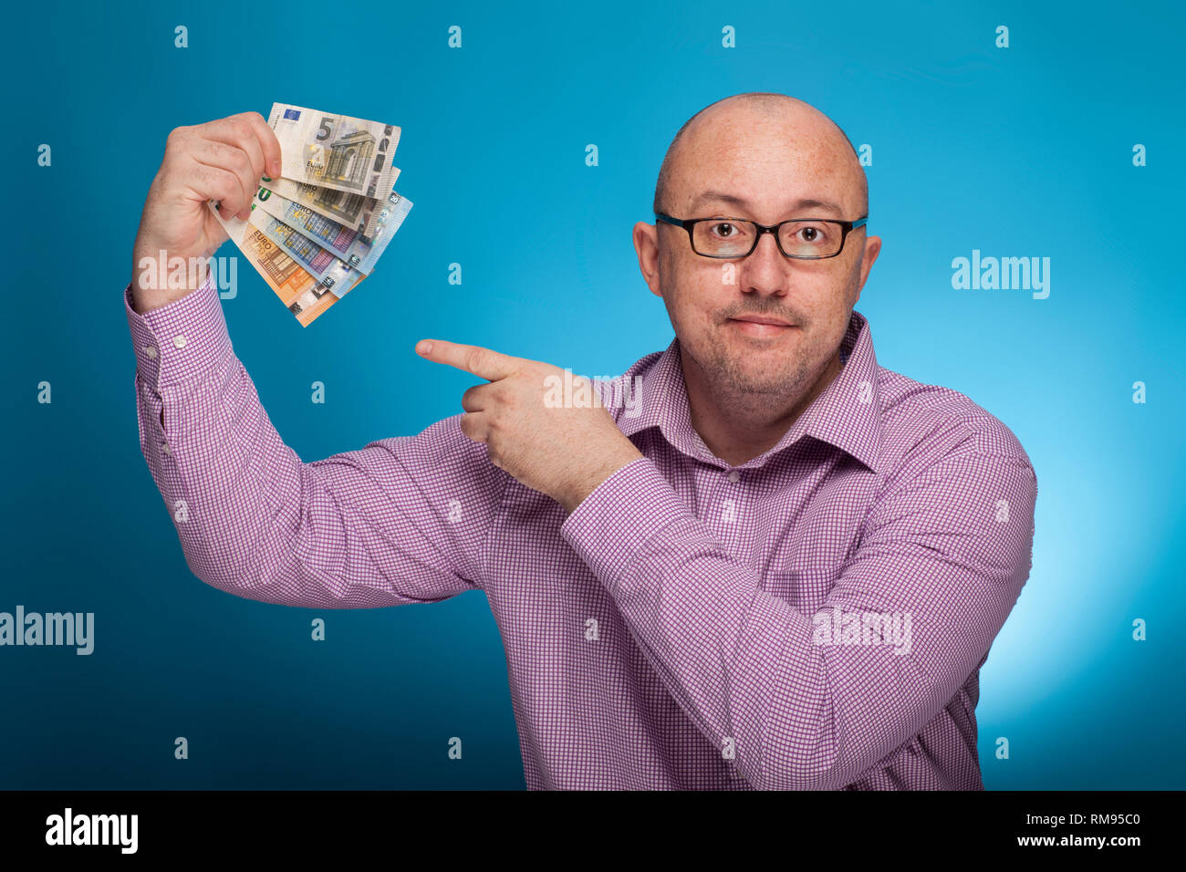 Un imprenditore in un spinaroli shirt puntando con il dito indice sul denaro contante in euro, su sfondo blu. Foto Stock