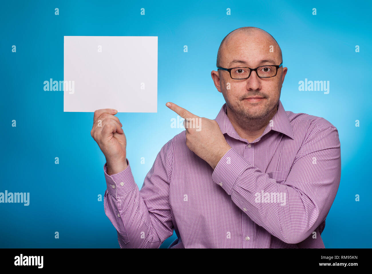 Un imprenditore in un spinaroli shirt mantiene un vuoto, bianco segno, segnaposto, su sfondo blu. Foto Stock