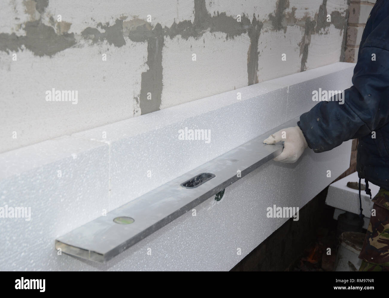 Builder installare styrofoam tavola di isolamento e la misurazione con livella a bolla. Esterno l'isolamento di spugna. Foto Stock