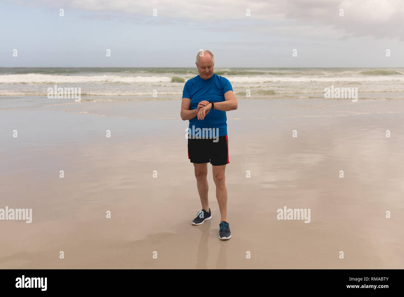 Felice l'uomo senior utilizzando smartwatch in spiaggia Foto Stock