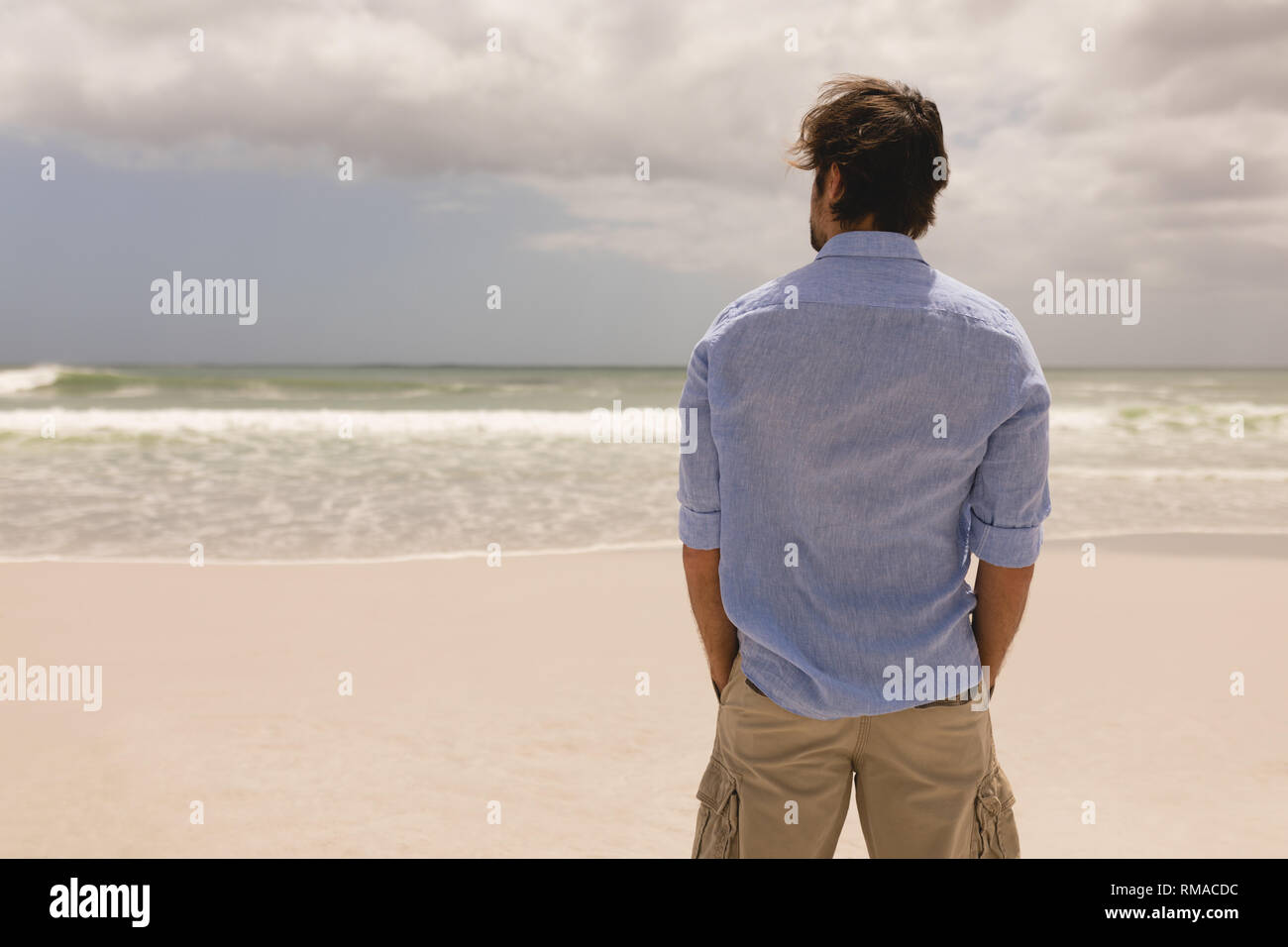 Uomo in piedi con le mani in tasca sulla spiaggia Foto Stock