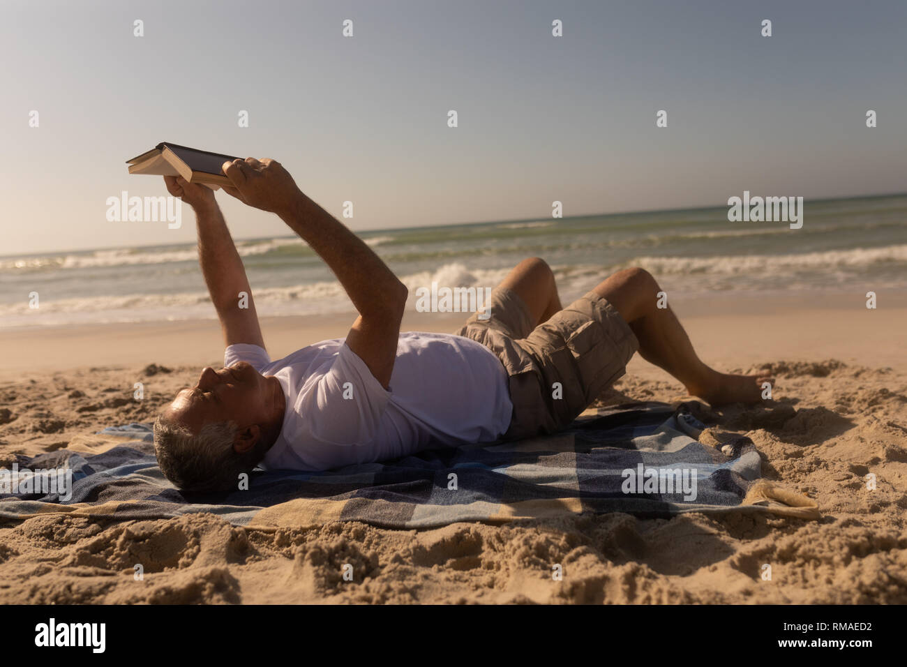 Senior uomo a leggere un libro mentre vi rilassate sulla coperta picnic in spiaggia Foto Stock