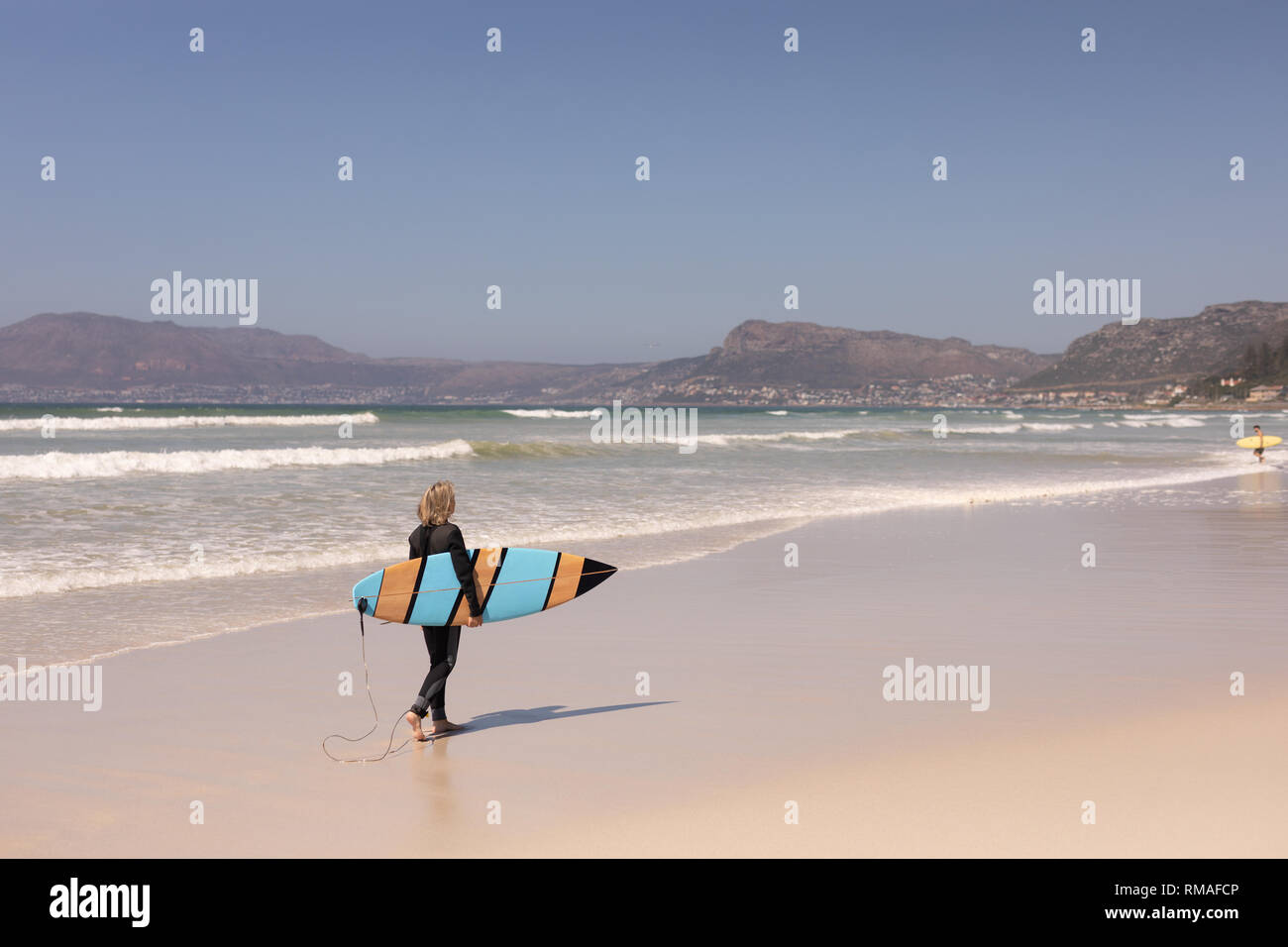 Vista posteriore senior surfista femmina a piedi con la tavola da surf in spiaggia Foto Stock