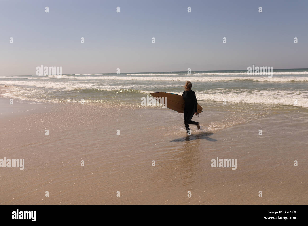 Senior surfista femmina a piedi con la tavola da surf in spiaggia Foto Stock