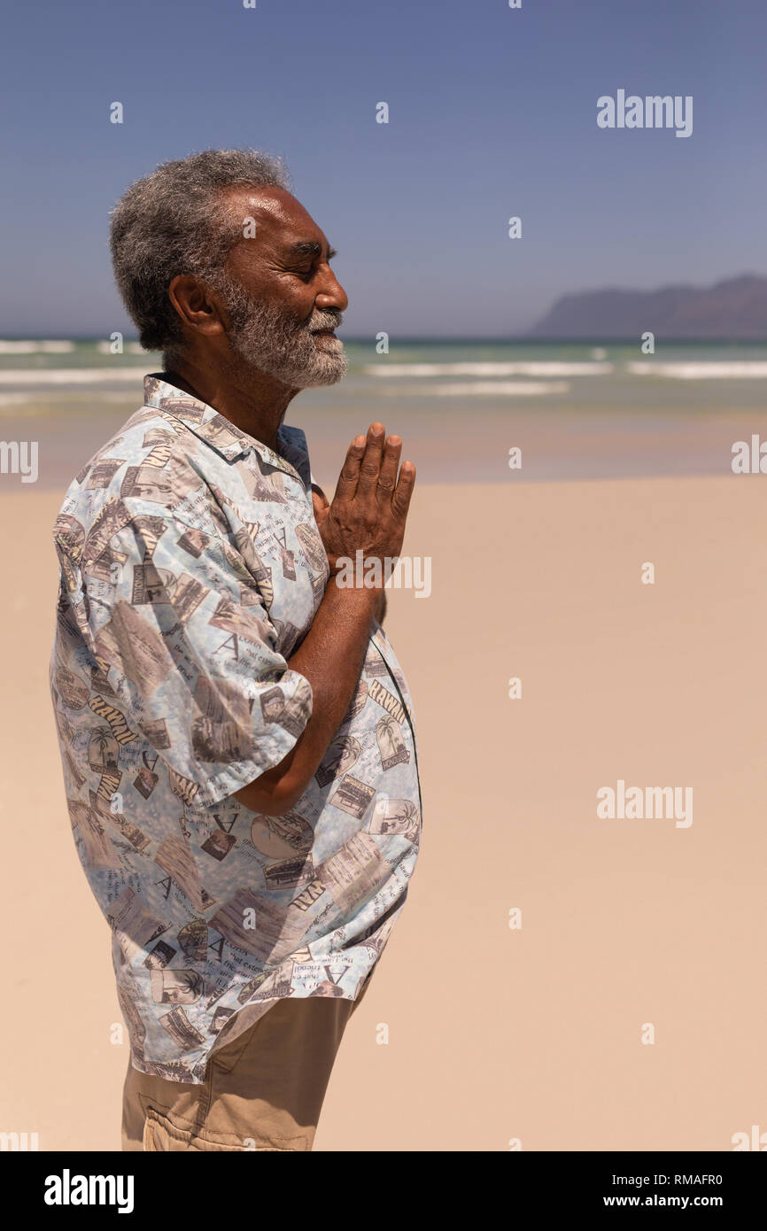 Senior uomo nero con mani giunte in preghiera sulla spiaggia Foto Stock