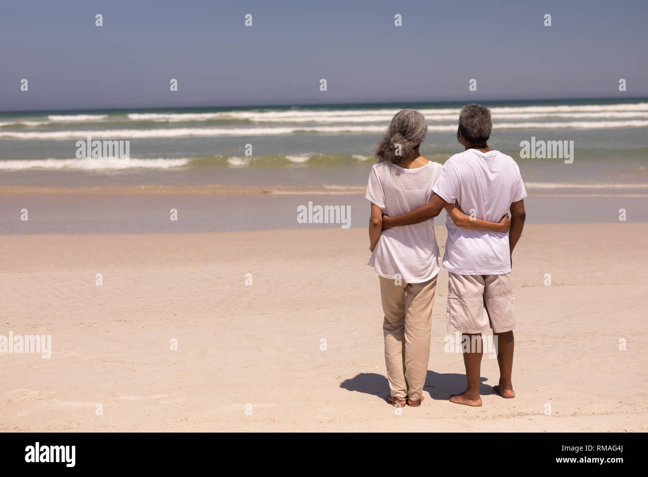 Coppia senior in piedi su una spiaggia con le braccia intorno a ciascun altro Foto Stock
