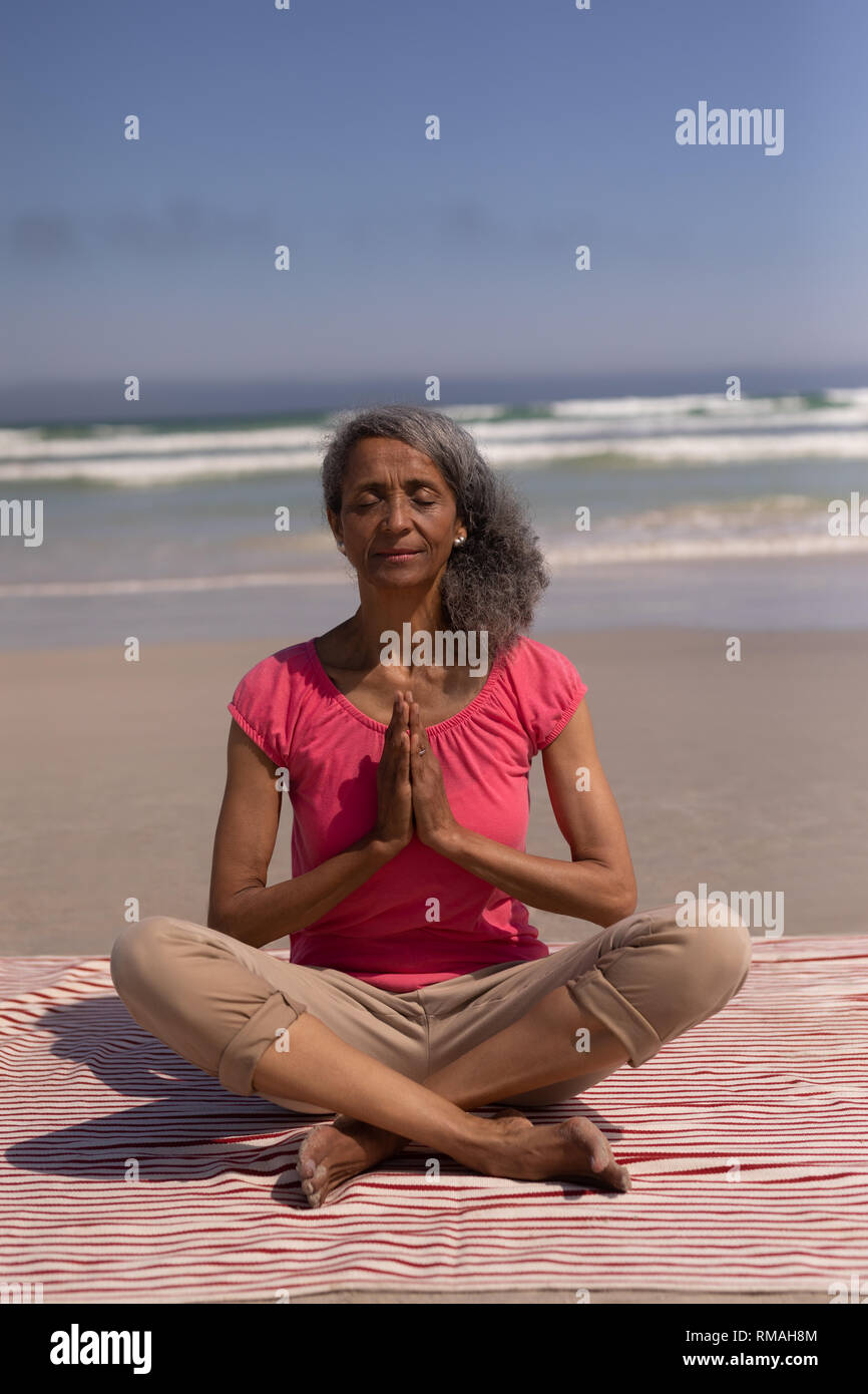 Senior donna con gli occhi chiusi e le mani incrociate fare yoga sulla spiaggia Foto Stock