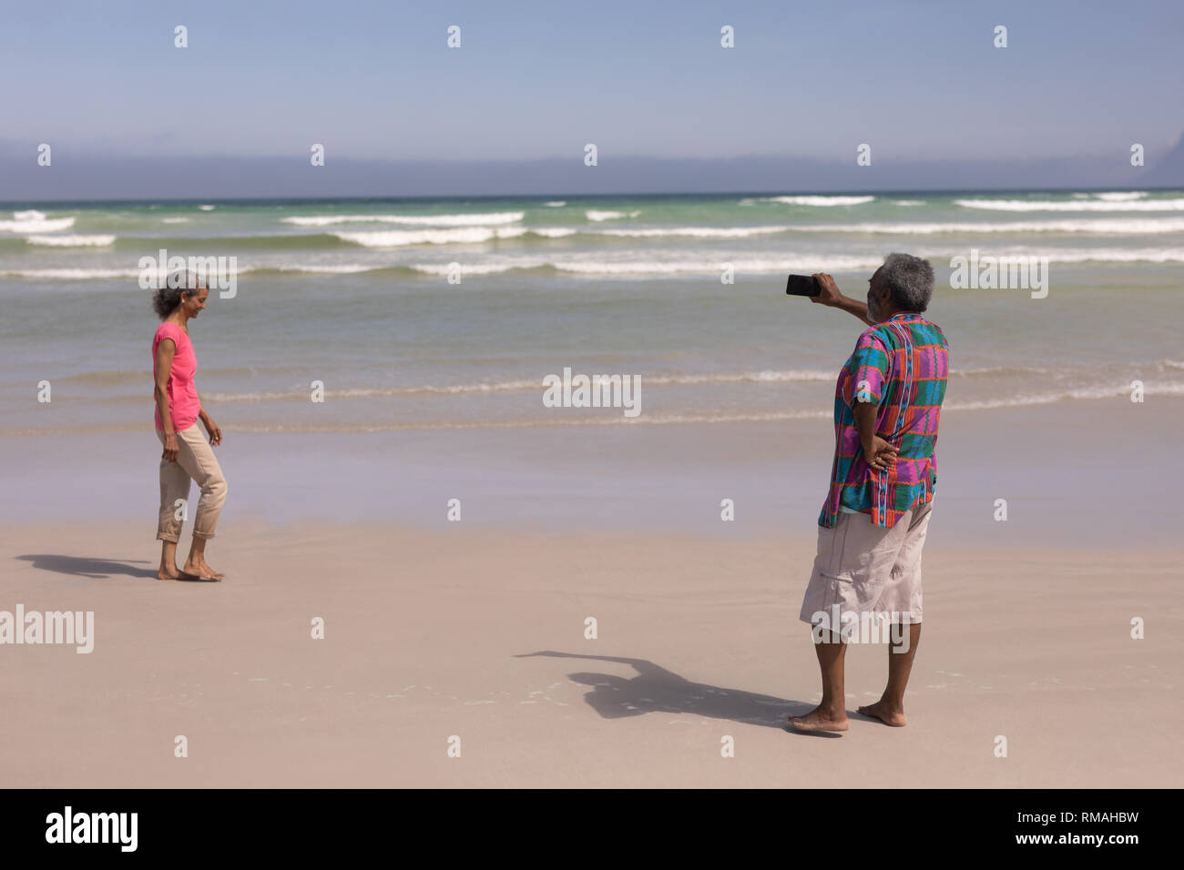 Senior uomo prendendo foto di donna senior con telefono cellulare sulla spiaggia Foto Stock