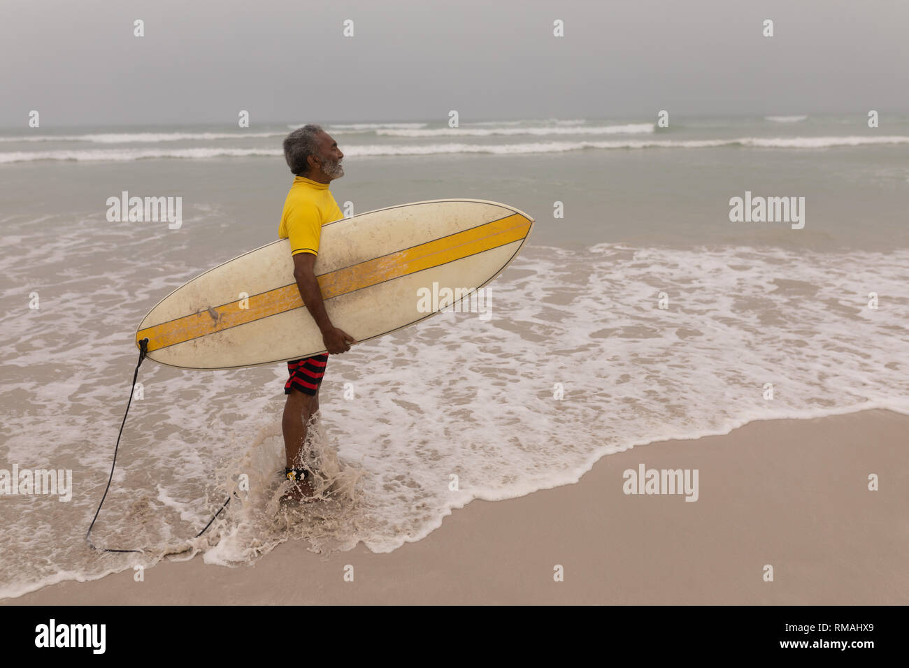 Senior surfista maschio con tavola da surf permanente sulla spiaggia Foto Stock