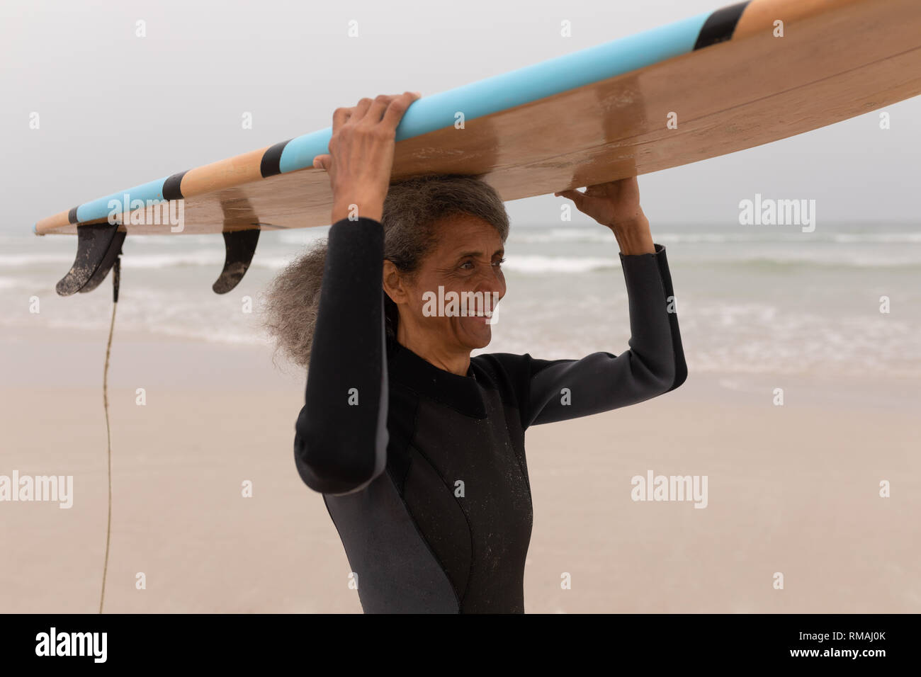 Senior surfista femmina che porta la tavola da surf sulla sua testa Foto Stock