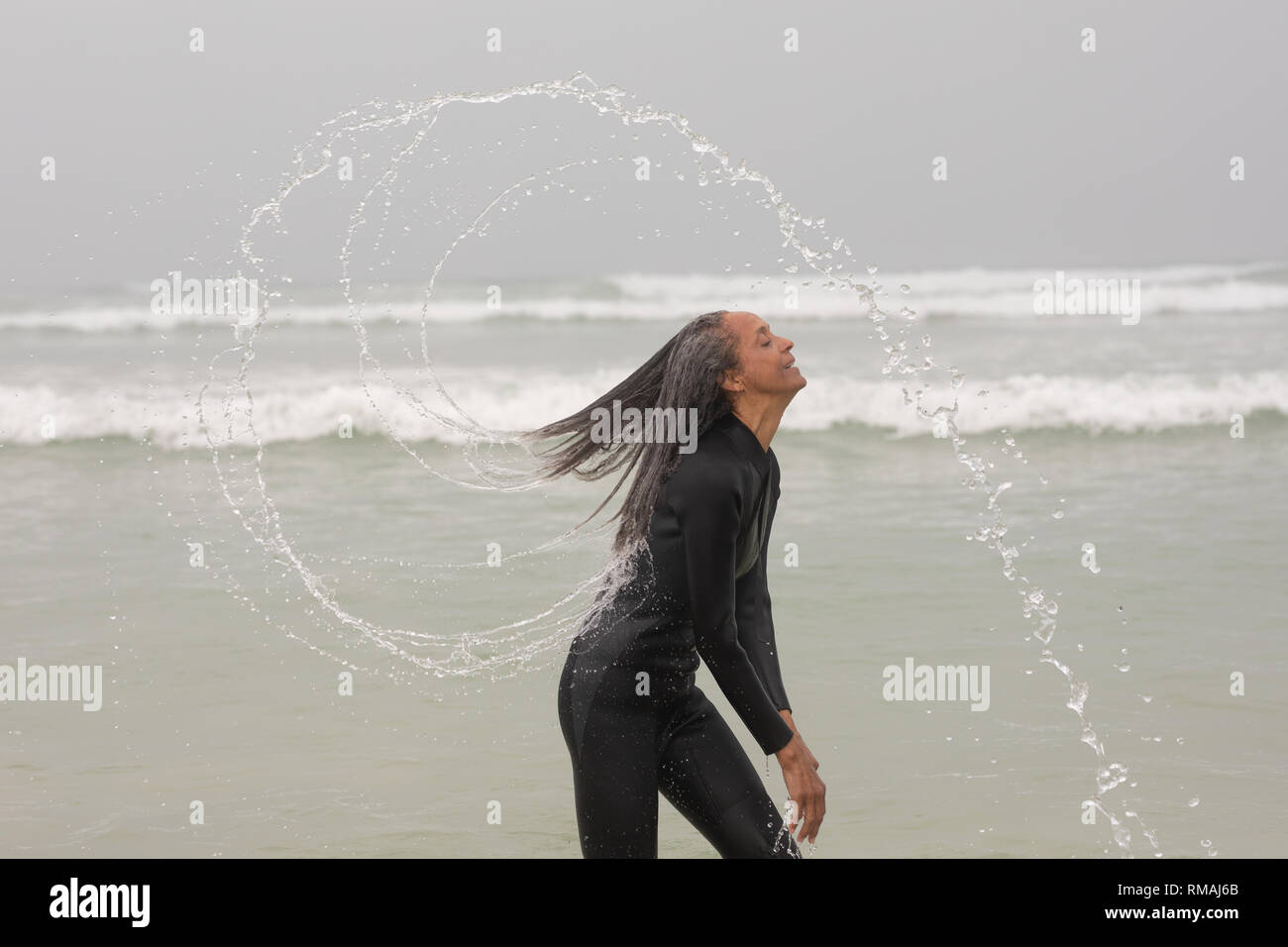 Felice femmina senior surfer spruzzi d'acqua con i suoi capelli presso la spiaggia di Foto Stock