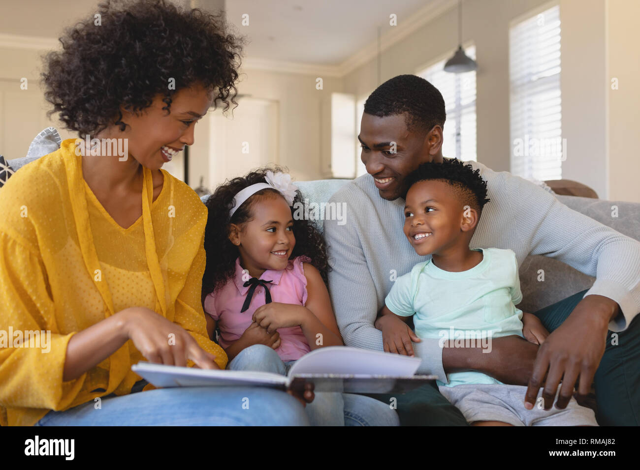 Felice americano africano i genitori con i loro bambini carino lettura storybook sul divano Foto Stock