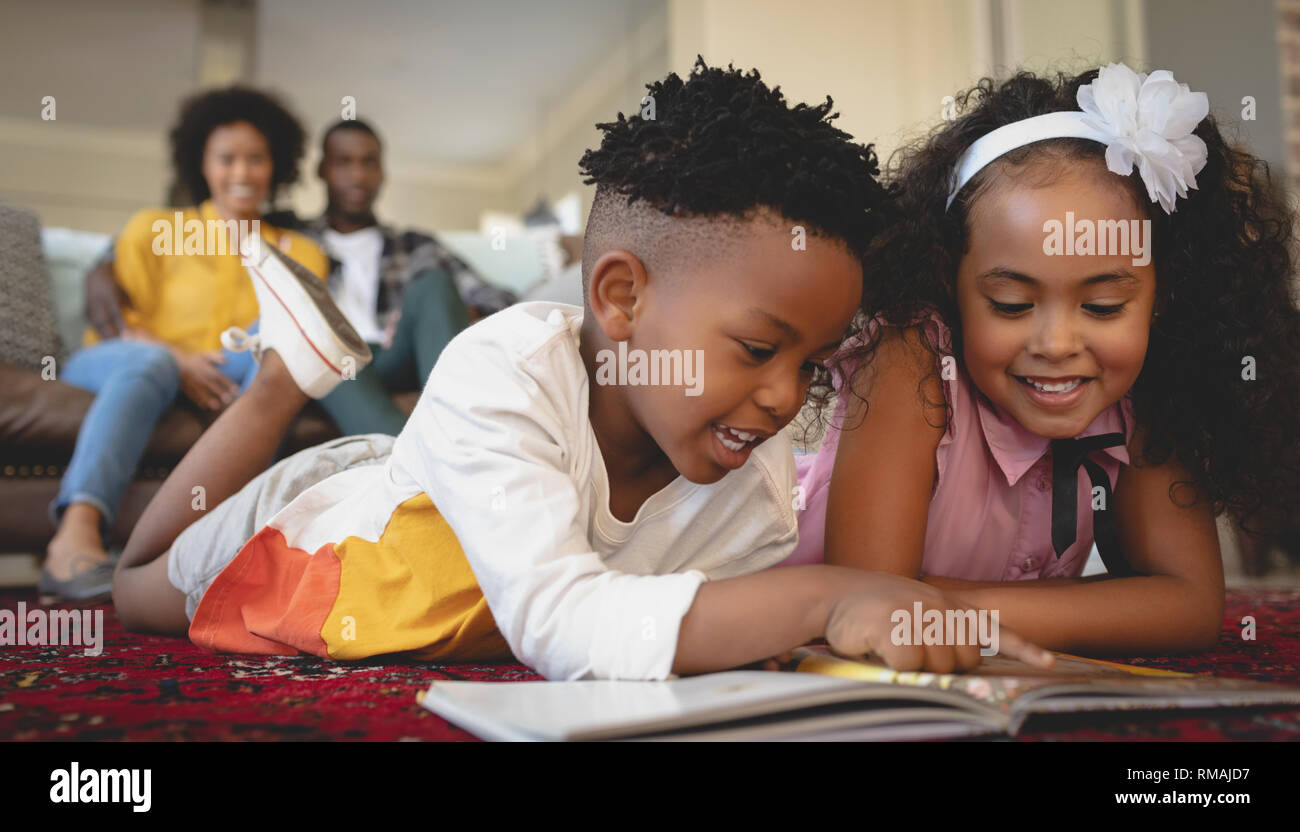 Carino americano africano i gemelli sdraiato sul pavimento e la lettura di un libro delle fiabe Foto Stock