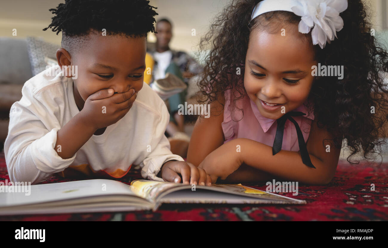 Carino americano africano i gemelli sdraiato sul pavimento e la lettura di un libro delle fiabe Foto Stock
