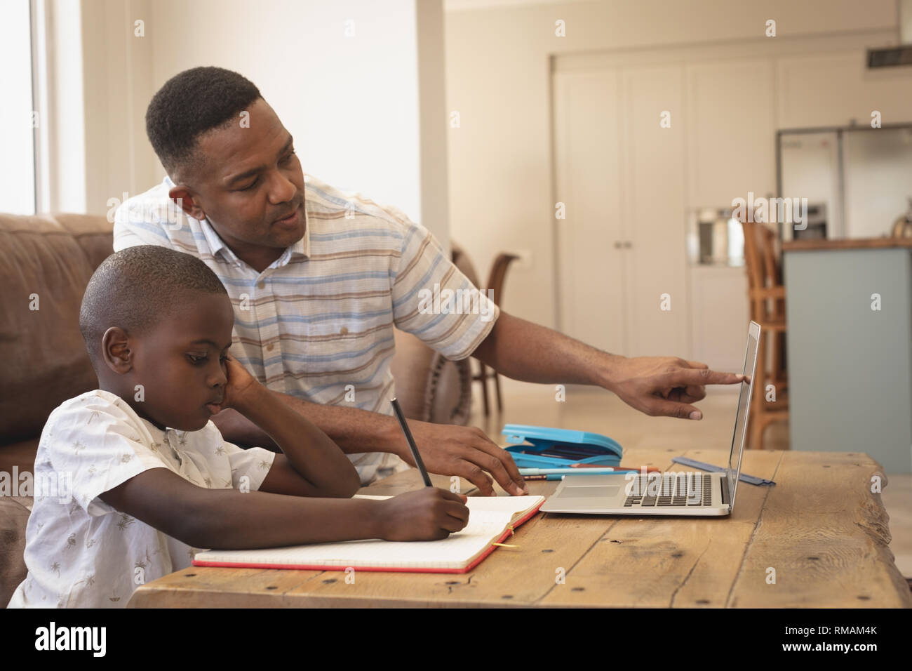 African American padre aiutando il suo figlio con i compiti di un portatile a tavola Foto Stock