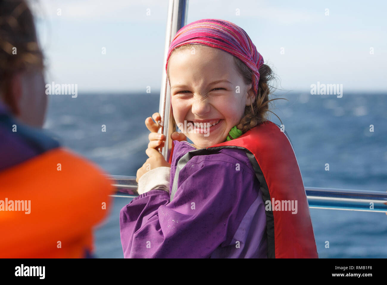 Ragazza sorridente in giacca di sicurezza a bordo di una barca. Famiglia su un blu whale watching viaggio. Foto Stock