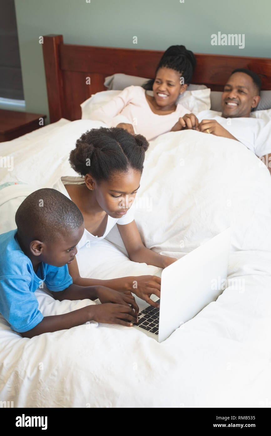 African American bambini utilizzando computer portatile mentre i genitori rilassante sul letto in camera da letto Foto Stock
