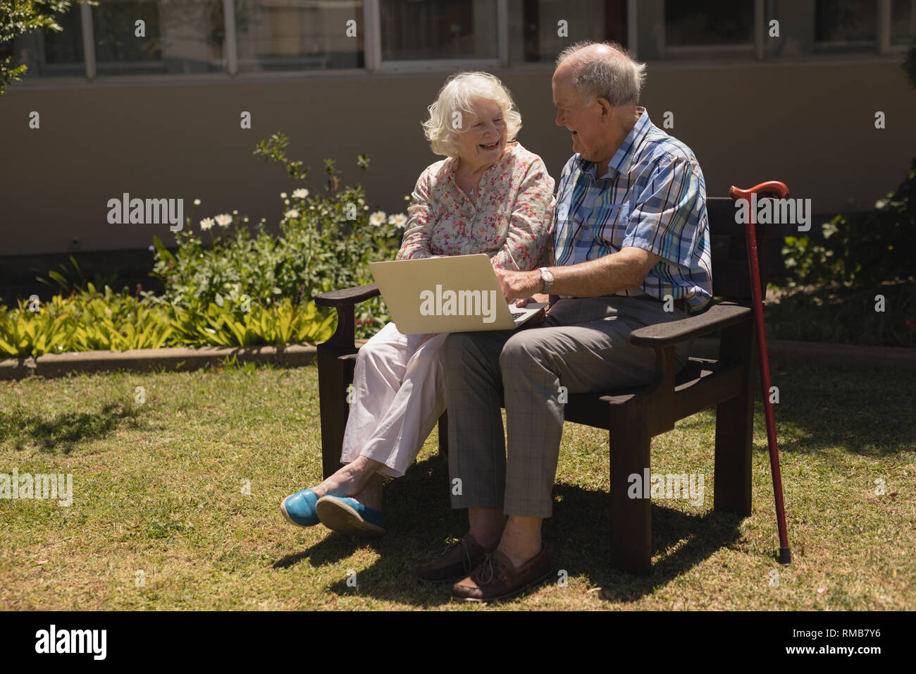 Vista frontale della coppia senior seduta sul banco di lavoro e utilizzo di computer portatile in giardino Foto Stock