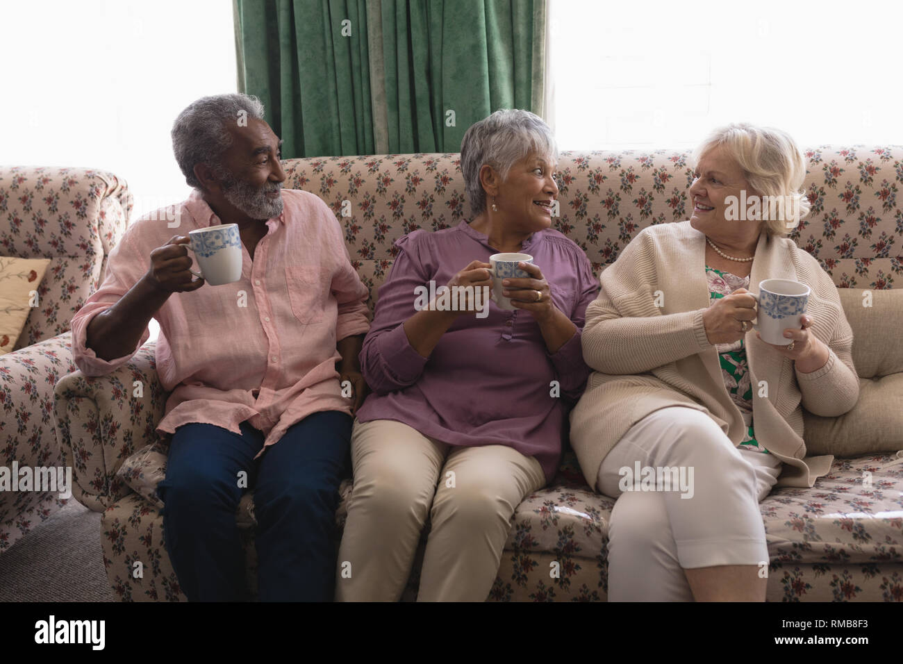 Senior persone che interagiscono con ogni altro pur avendo caffè nella stanza vivente Foto Stock