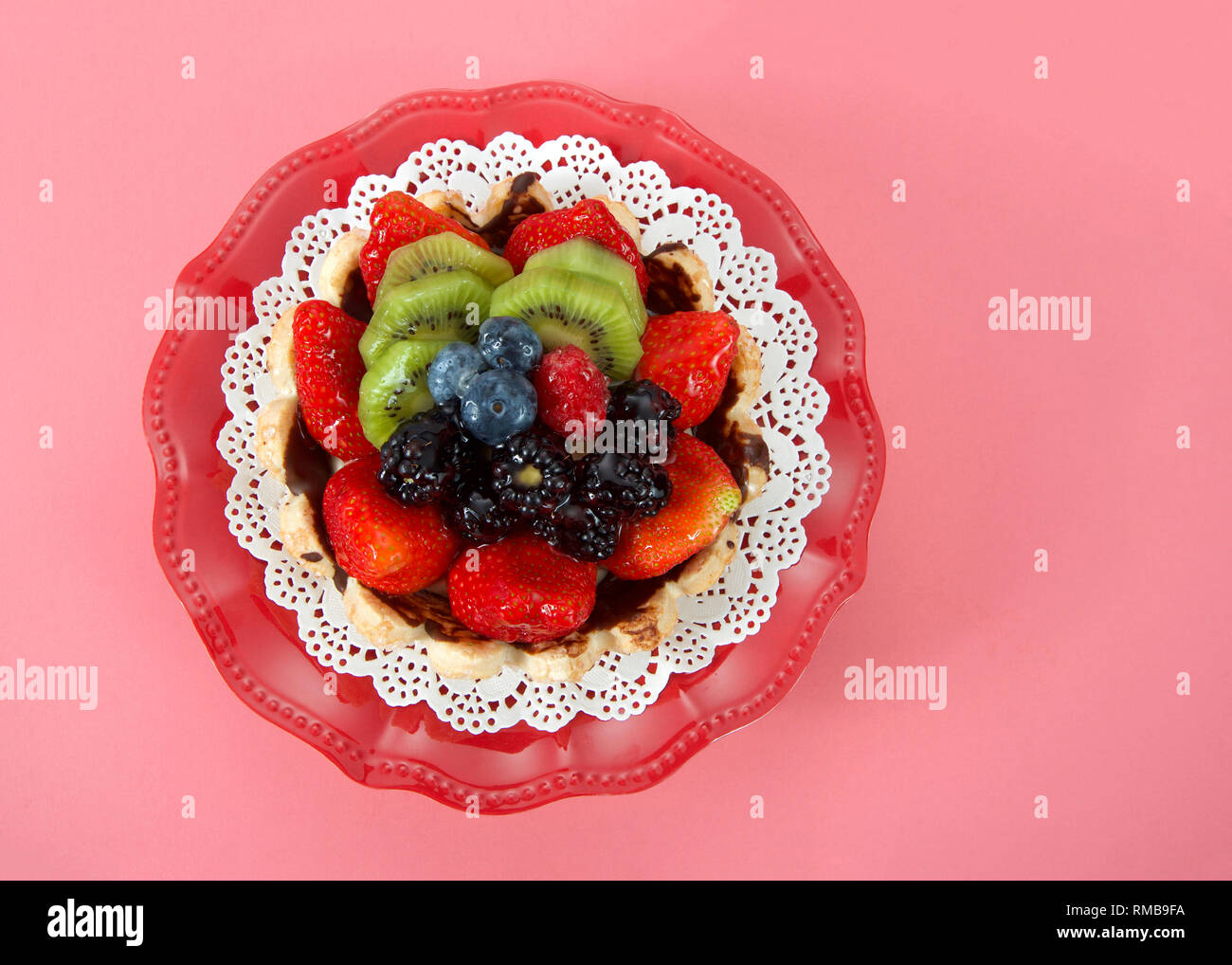 Frutta estiva fresca crostata con fragole, kiwi, mirtilli, "boysenberries" su un centrino bianco sulla piastra di rosso sfondo rosa. Vista superiore piatta. laici Foto Stock