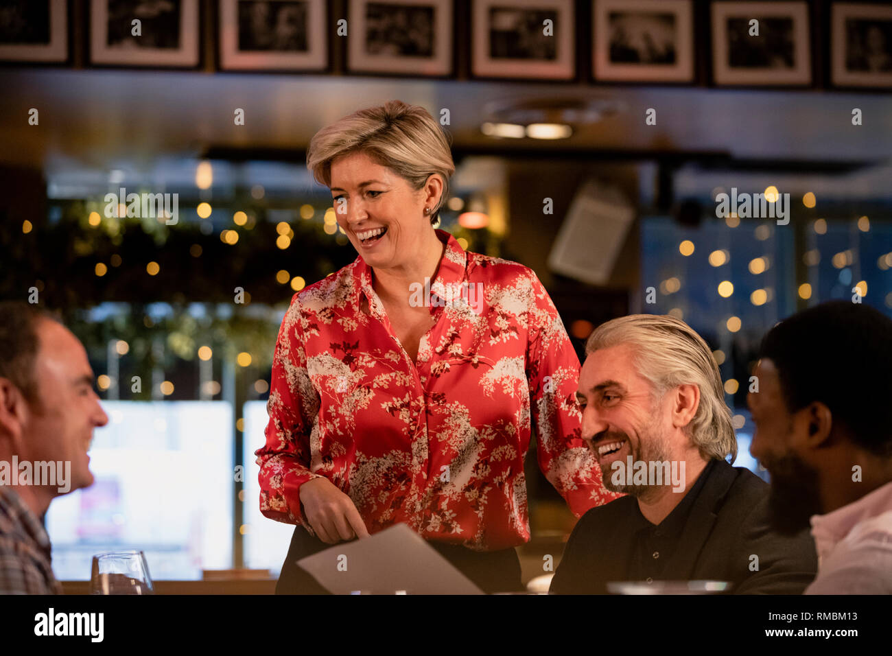 Sorridente cameriera maturo prendendo un ordine di cibo da un piccolo gruppo di metà uomini adulti in un ristorante. Foto Stock