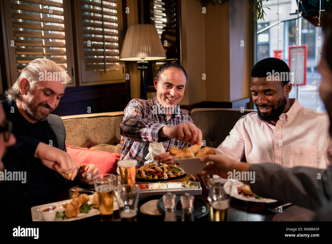 Piccolo gruppo di metà uomini adulti godendosi un po' di cibo. Un uomo è stato offerto un chip da parte di uno dei suoi amici. Foto Stock