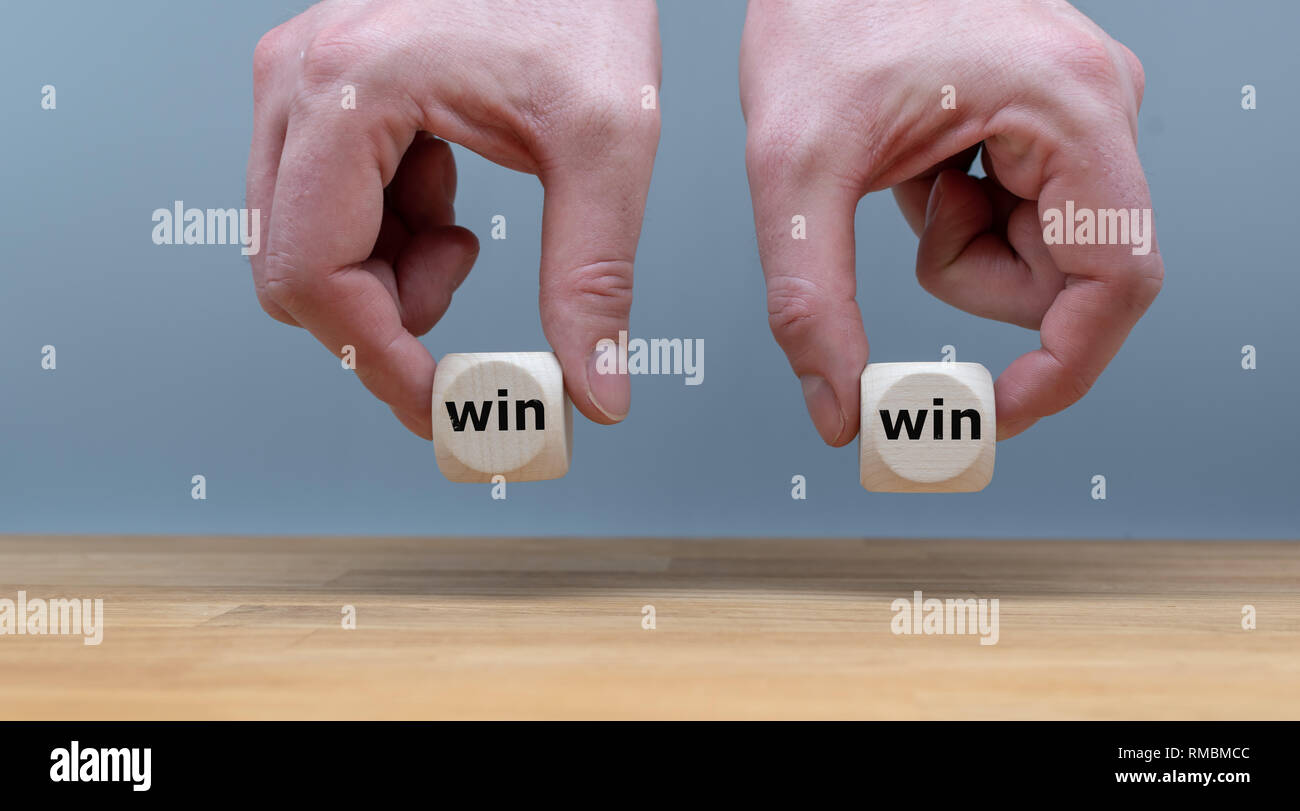 Simbolo per un win win situazione. Le mani sono tenendo due dadi con le parole 'win' e 'win' davanti a uno sfondo grigio. Foto Stock