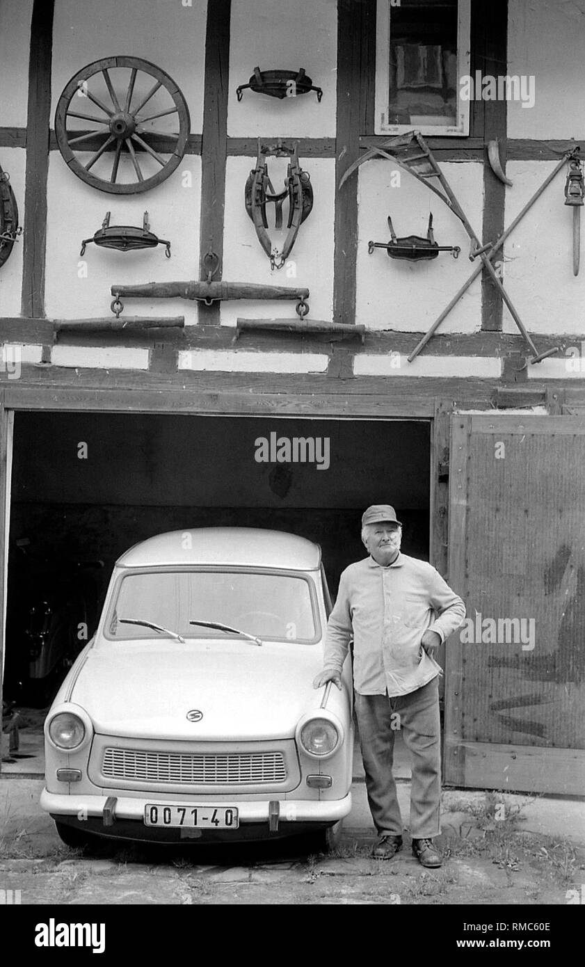 Un uomo è appoggiata contro il suo Trabant davanti a una casa in legno e muratura, intorno al 1979. Foto Stock