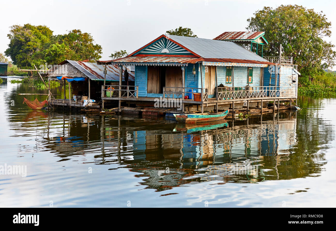 Tonlé Sap Lago, Cambogia. 19 dicembre 2017. Coloratissima casa galleggiante con alberi dietro e una barca di legno nella parte anteriore. Foto: Bryan Watt Foto Stock