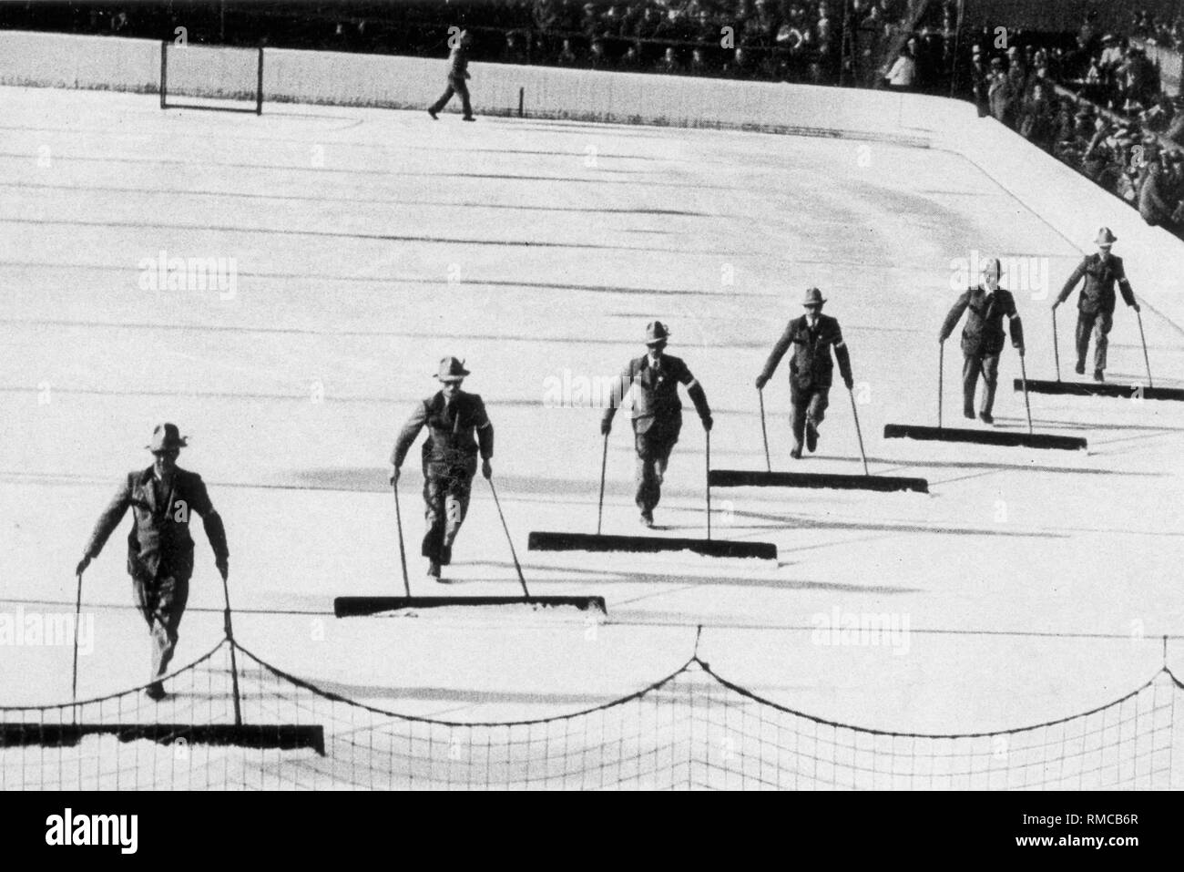 Olimpiadi invernali di Garmisch-Partenkirchen: neve mestolone in costume di Werdenfelser la pulizia della superficie del ghiaccio del ghiaccio artificiale stadium, accompagnato dalla vivace musica. Foto Stock