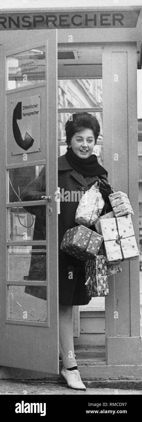 La donna porta pacchi di Natale lascia una cabina telefonica, 50s Foto Stock