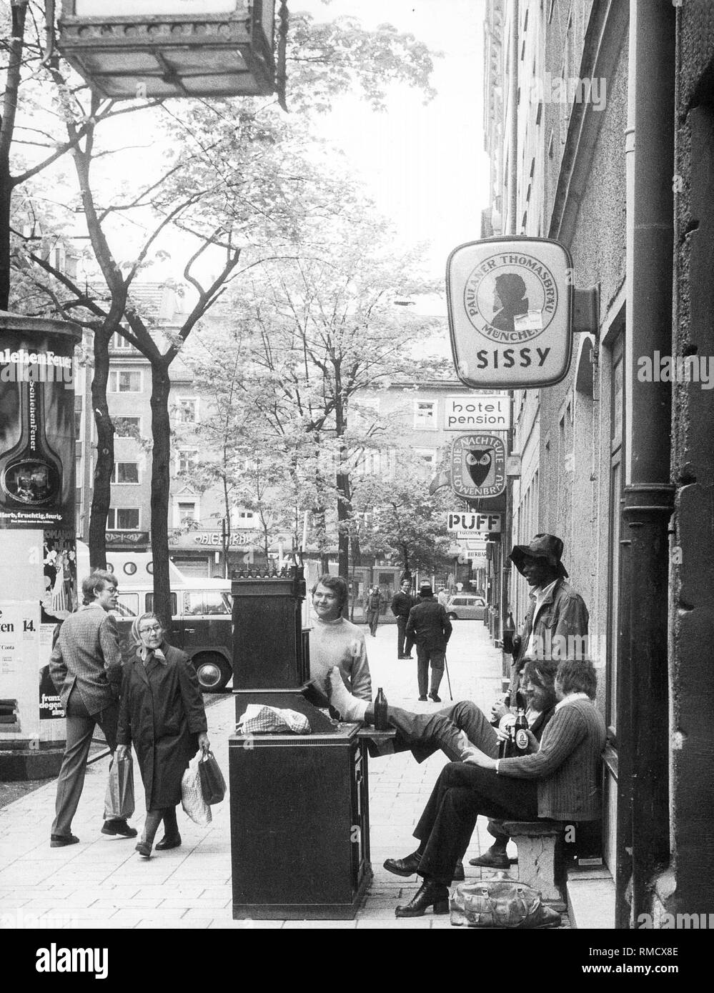 Giovani sit in Occamstrasse in Monaco di Baviera quartiere di Schwabing davanti ai loro liquor cabinet, sul quale sono candele accese. Un anziano passante guarda le vicende. Foto Stock