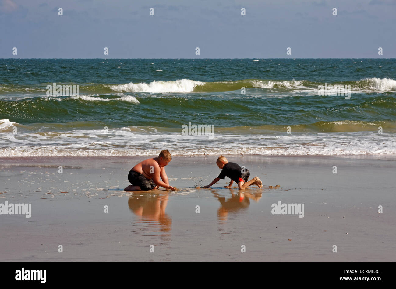 2 ragazzi di scavare, giocando, sabbia bagnata, acqua; Oceano Atlantico; onde; divertimento; gli amici, navigare, costa, Ormond Beach; FL; Florida; autunno; orizzontale Foto Stock