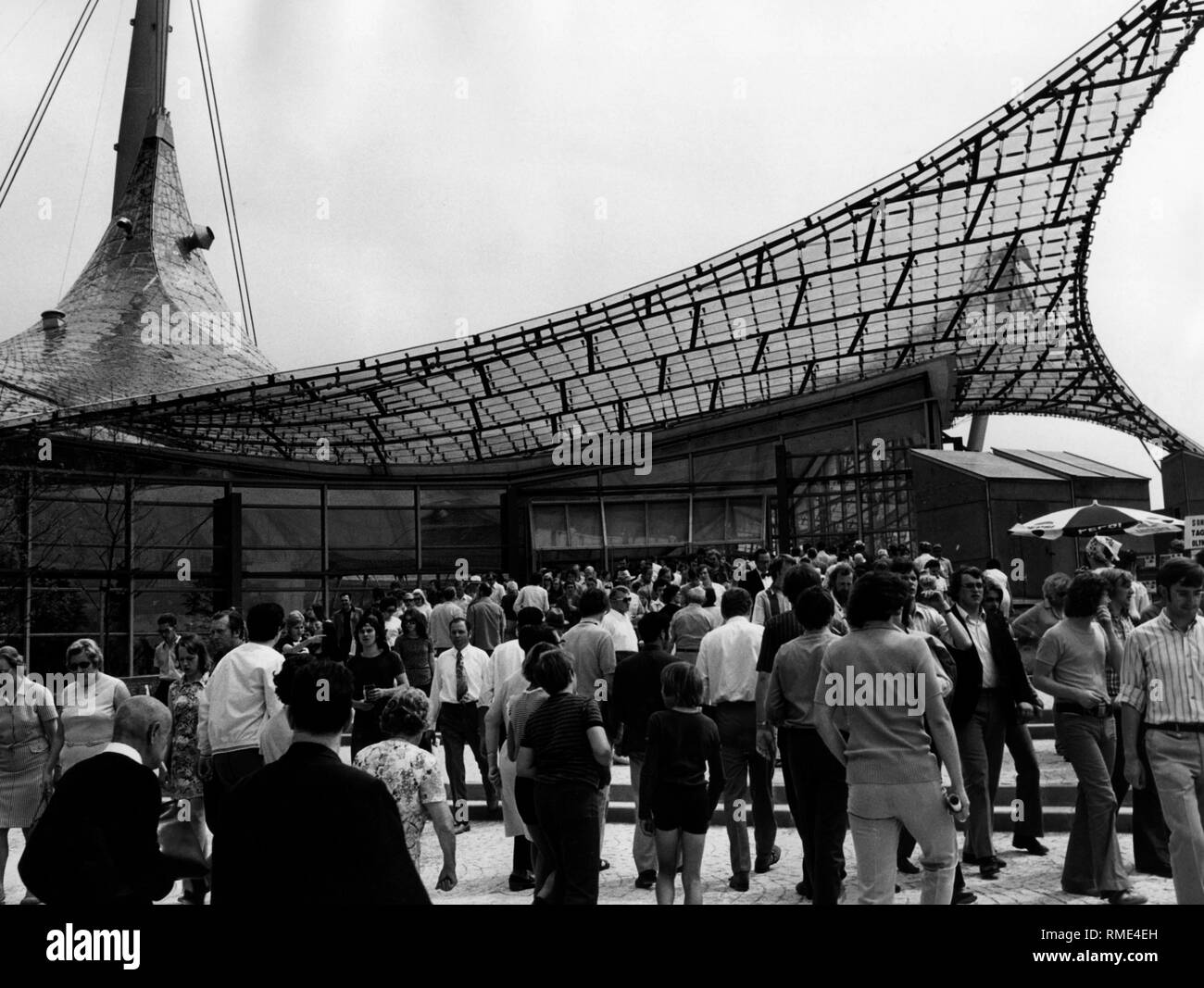 I visitatori a Monaco di Baviera al Parco Olimpico di fronte all'Olympiahalle. A destra un ombrello promozionale della società "Pepsi'. Foto Stock